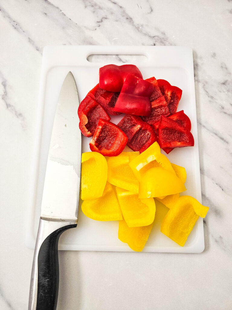 Chopped red and yellow bell peppers on a white cutting board with a chef’s knife.