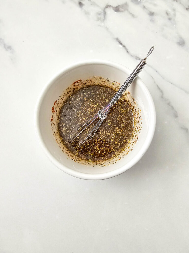 Fully mixed marinade with herbs and spices whisked together in a bowl.