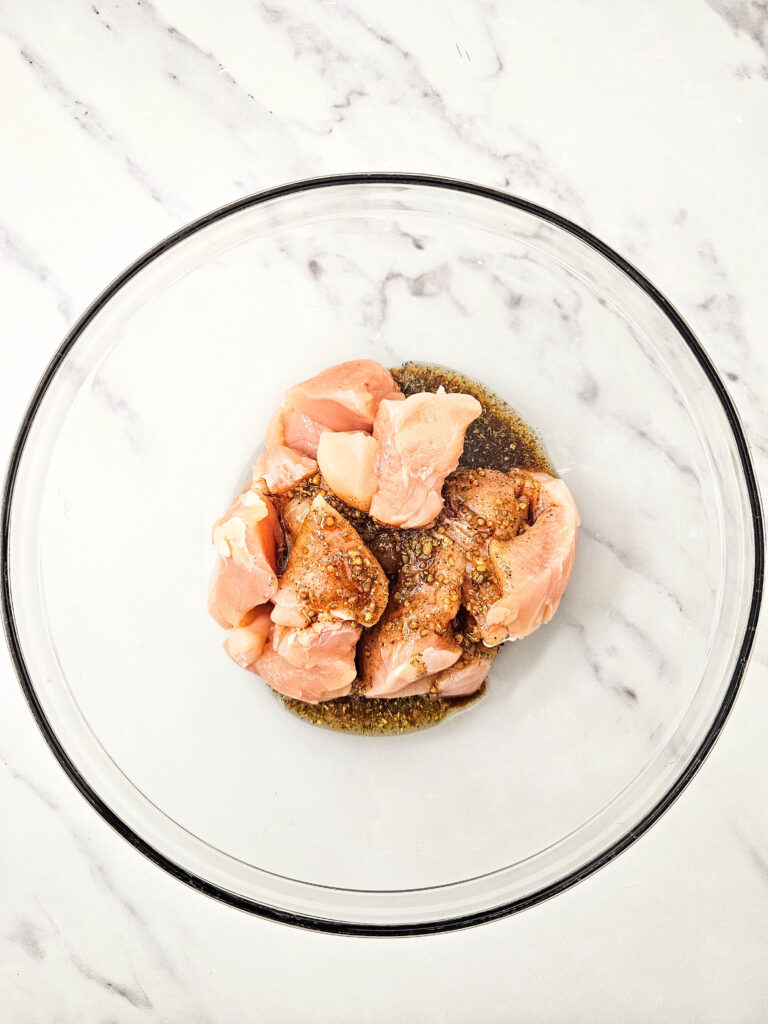 Raw chicken pieces added to marinade in a glass mixing bowl.