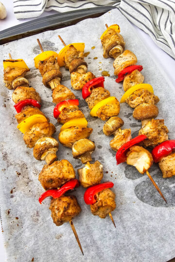 Golden brown chicken kabobs with roasted vegetables on a sheet pan.