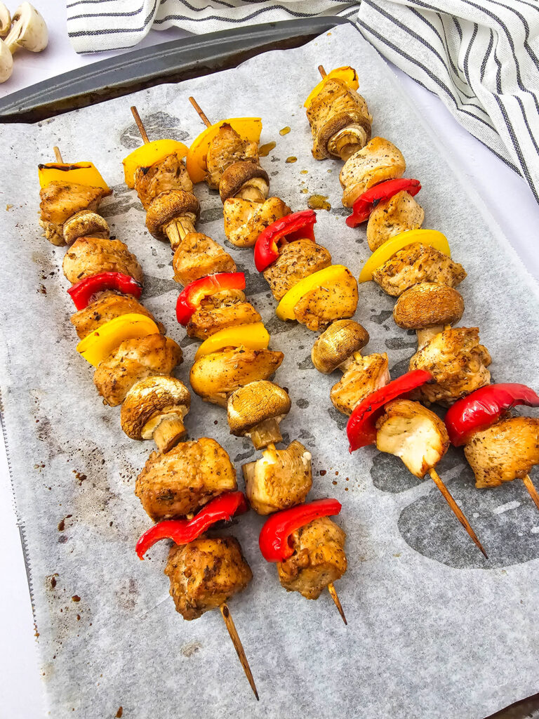 Golden brown chicken kabobs with roasted vegetables on a sheet pan.
