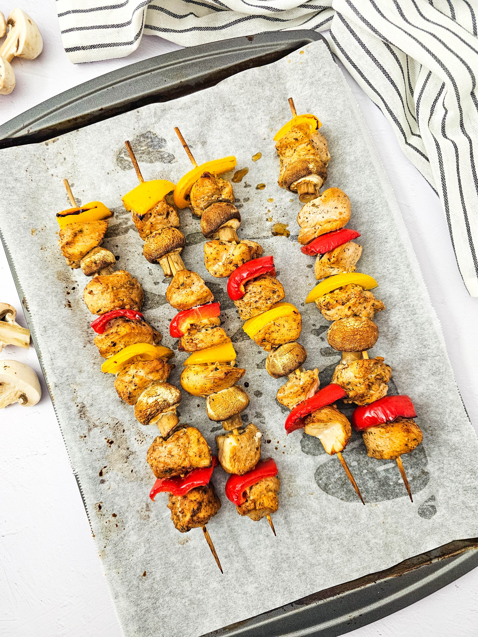 Golden brown chicken kabobs with roasted vegetables on a sheet pan.